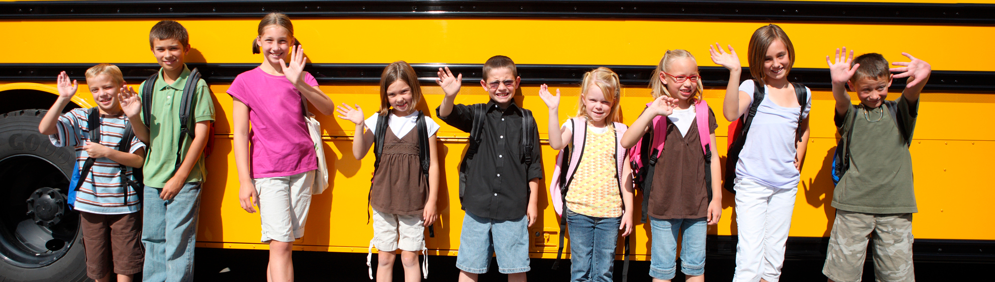 students standing in front of a bus waving